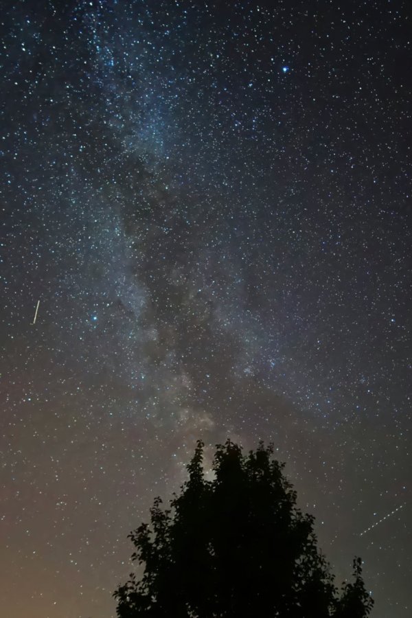 A picture of a pristine night sky. Many stars are visible along with the disk of the Milky Way. Several satellite streaks are visible within the image